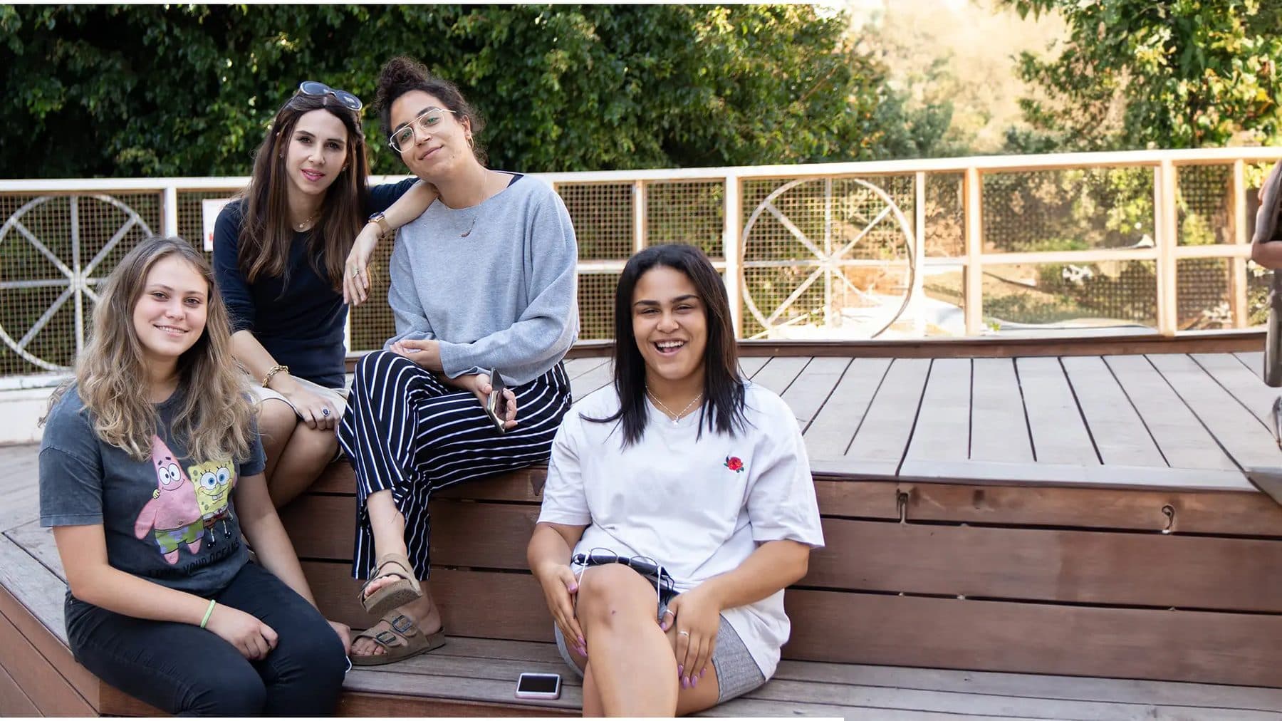 בנות שירות יושבות יחד על דק עץ ומחייכות